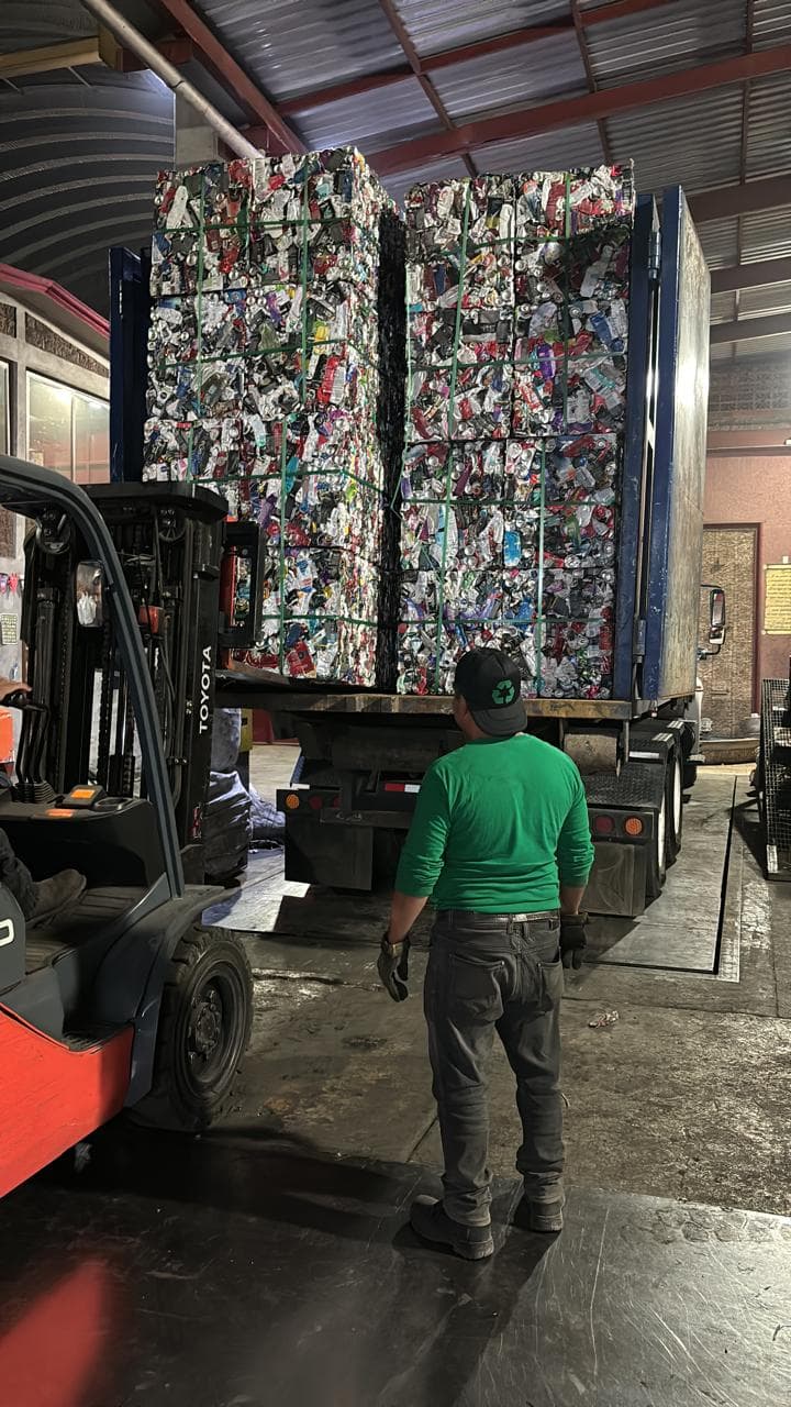 Operario observa un montacargas cargando fardos de latas de aluminio compactadas en un camión.