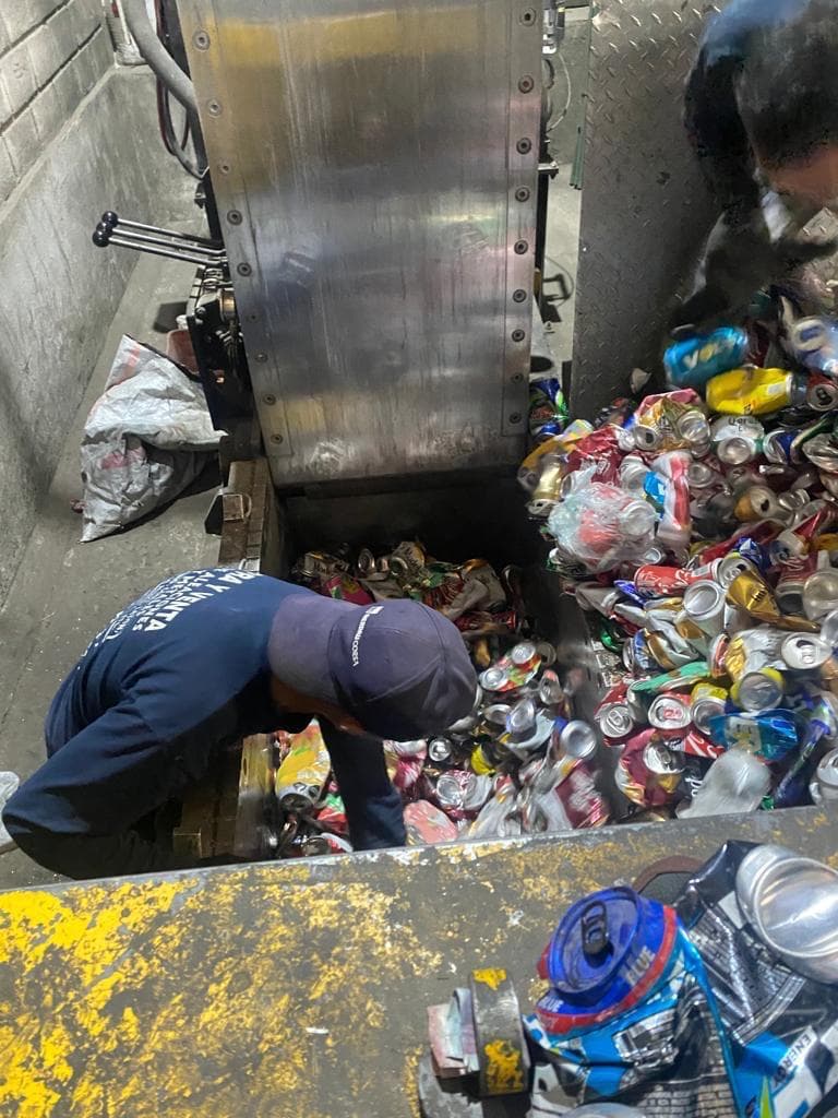 Un trabajador clasifica y procesa latas de aluminio recicladas en una máquina compactadora industrial.